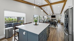 Une cuisine spacieuse dotée d’un grand îlot central, de poutres en bois et offrant une vue sur l’extérieur.