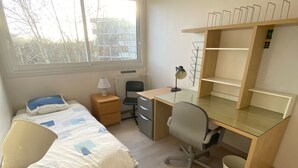 A bedroom with a bed, desk, chair, and a window.