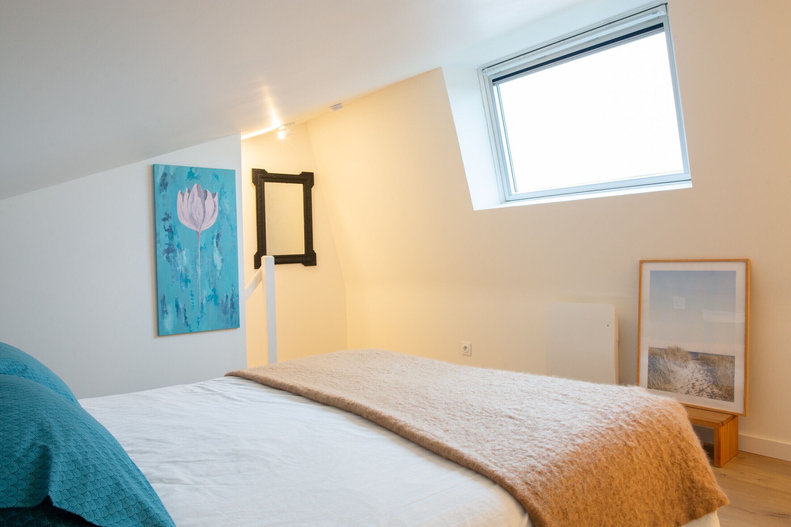 Un dormitorio con cama, ventana y obras de arte en las paredes.