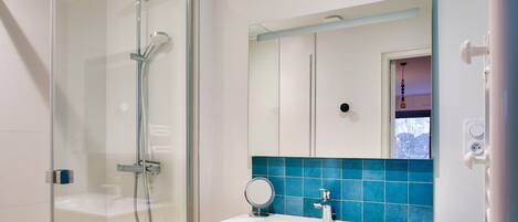 A modern bathroom with a glass-enclosed shower, a white sink, a mirror, and a blue-tiled backsplash.