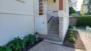 Uma casa com varanda, escadas e um pequeno jardim.