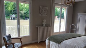 Quarto com uma grande janela, um radiador, uma escultura de busto e uma cama com um cobertor verde.