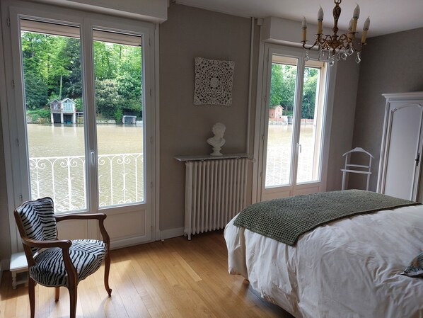 Une chambre avec une grande fenêtre, un radiateur, un buste sculpté et un lit recouvert d’une couverture verte.