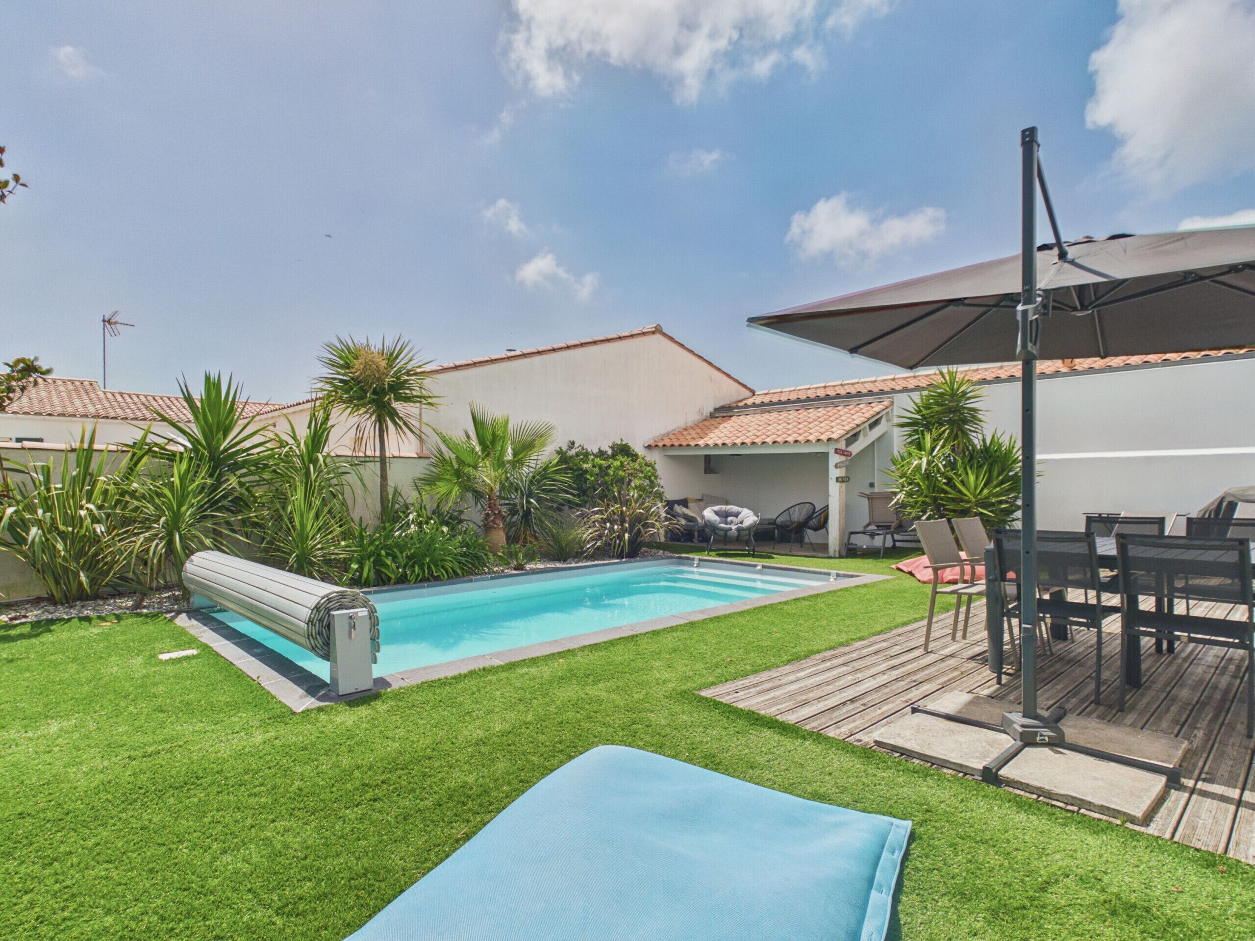 A swimming pool surrounded by a grassy lawn, with a patio area and outdoor furniture.