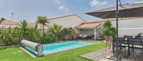 A swimming pool surrounded by a grassy lawn, with a patio area and outdoor furniture.