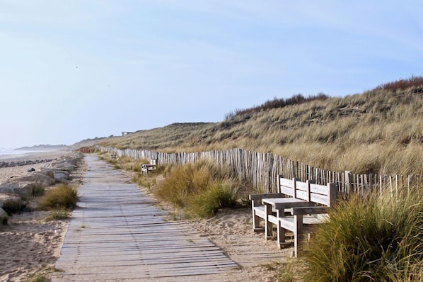 A wooden boardwalk leading to a beach, with benches and a wooden fence along the path.