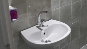 Une salle de bain avec un lavabo blanc, un meuble à pharmacie en bois et des carreaux gris.