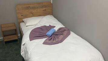 Una cama bien hecha con cabecera de madera, una mesita de noche de madera y una alfombra estampada.