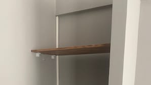 Un placard d’angle avec deux étagères en bois et une porte blanche.