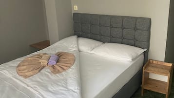 Un lit bien fait, avec une tête de lit grise, une table de chevet en bois et un tapis à motifs verts.