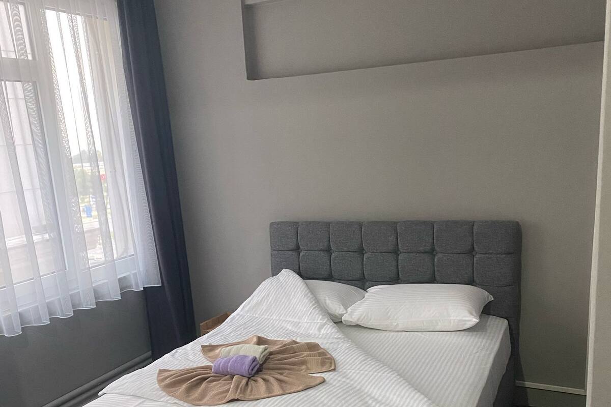 A neatly made bed with a grey headboard, a white comforter, and a brown throw blanket.