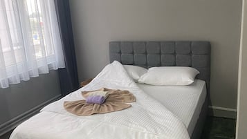 A neatly made bed with a grey headboard, a white comforter, and a brown throw blanket.