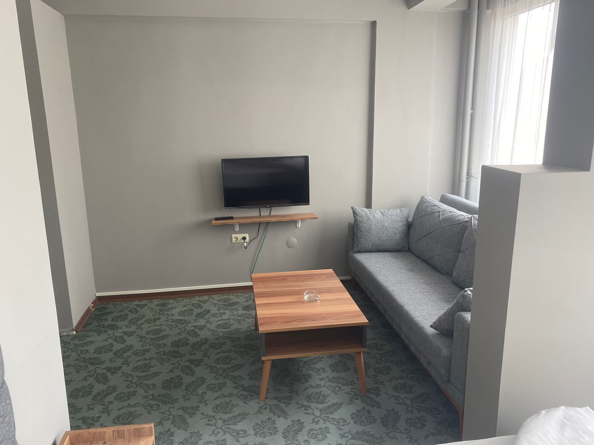Una habitación pequeña y moderna con un sofá gris, una mesita de madera y un televisor montado.