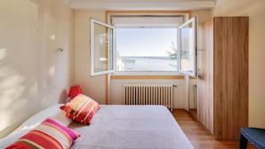 A bedroom with a bed, a window, a radiator, and a wardrobe.