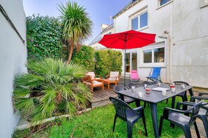 Une terrasse avec une table, des chaises et un parasol rouge.