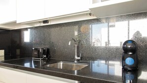 Eine Küche mit schwarzer Granitabdeckung, einer Edelstahlspüle, einer schwarzen Kaffeemaschine und einem schwarzen Wasserkocher.