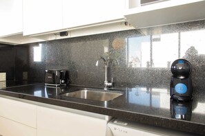 A kitchen with a black granite countertop, a stainless steel sink, a black coffee maker, and a black electric kettle.