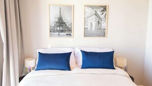 Ein Hotelzimmer mit einem Bett, zwei blauen Kissen, einer weißen Decke und zwei gerahmten Bildern an der Wand.
