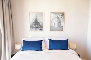 Une chambre d’hôtel avec un lit, deux oreillers bleus, une couette blanche et deux tableaux encadrés accrochés au mur.
