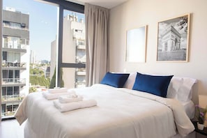 Une chambre d’hôtel avec un grand lit, une vue sur la ville et deux tableaux encadrés au mur.