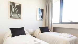 Une chambre d’hôtel avec deux lits, chacun étant équipé d’un oreiller et d’une serviette pliée. Deux tableaux encadrés sont accrochés au mur.