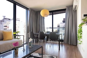 Un salon moderne comprenant un canapé, une table à manger, des chaises et une grande fenêtre avec des rideaux.
