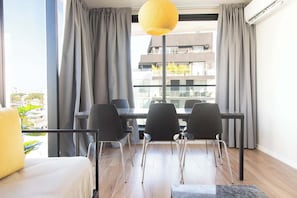 Une chambre d’hôtel moderne avec une grande fenêtre, une table à manger avec des chaises et un luminaire suspendu jaune.