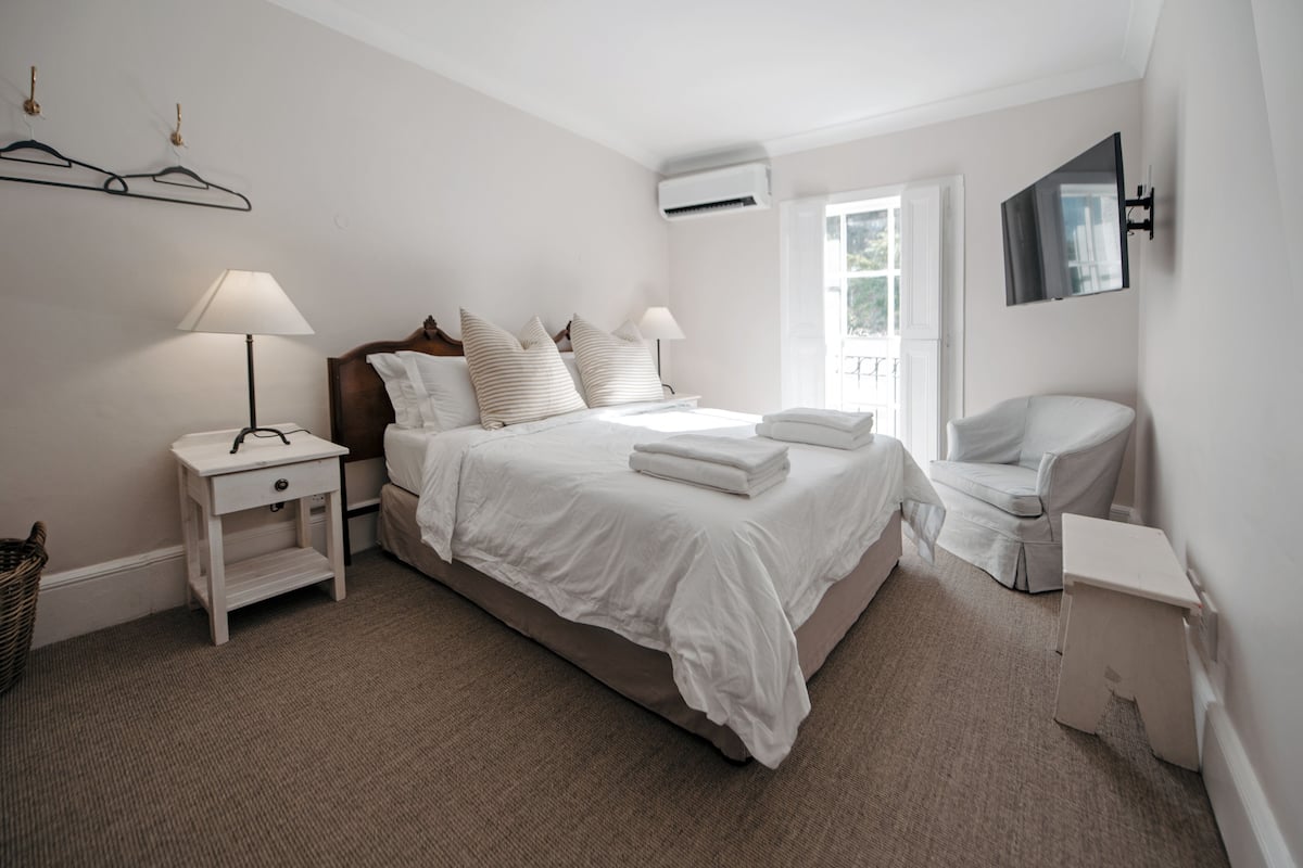 Quarto bem arrumado com cama, mesas de cabeceira, uma cadeira e um espelho.