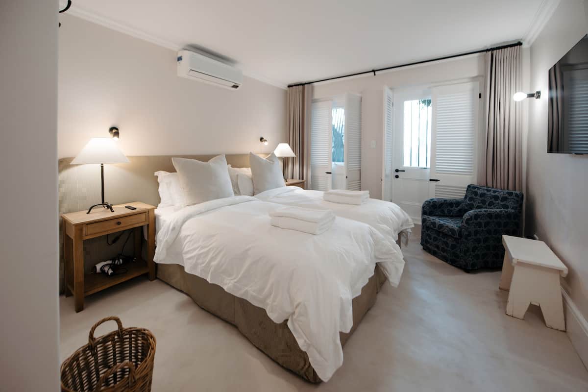 Quarto de hotel com cama grande, mesas de cabeceira, uma cadeira, um banquinho e uma cesta.