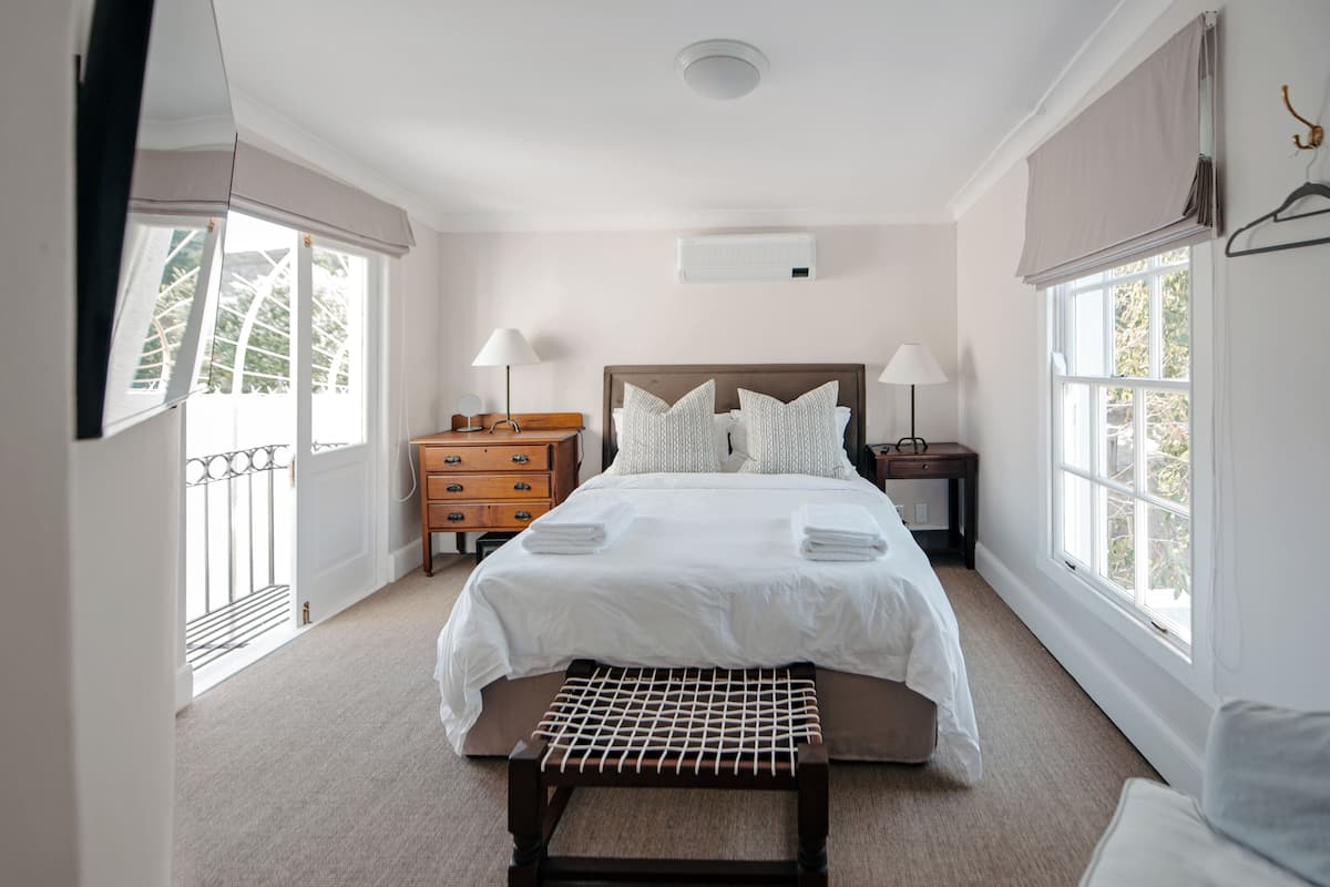Um quarto bem arrumado, com uma cama grande, mesas de cabeceira e um banco.