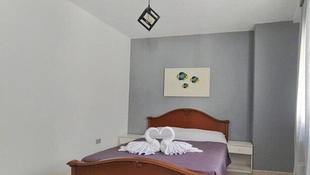 Een slaapkamer met een houten bed, een witte nachtkastje en een kunstwerk aan de muur.