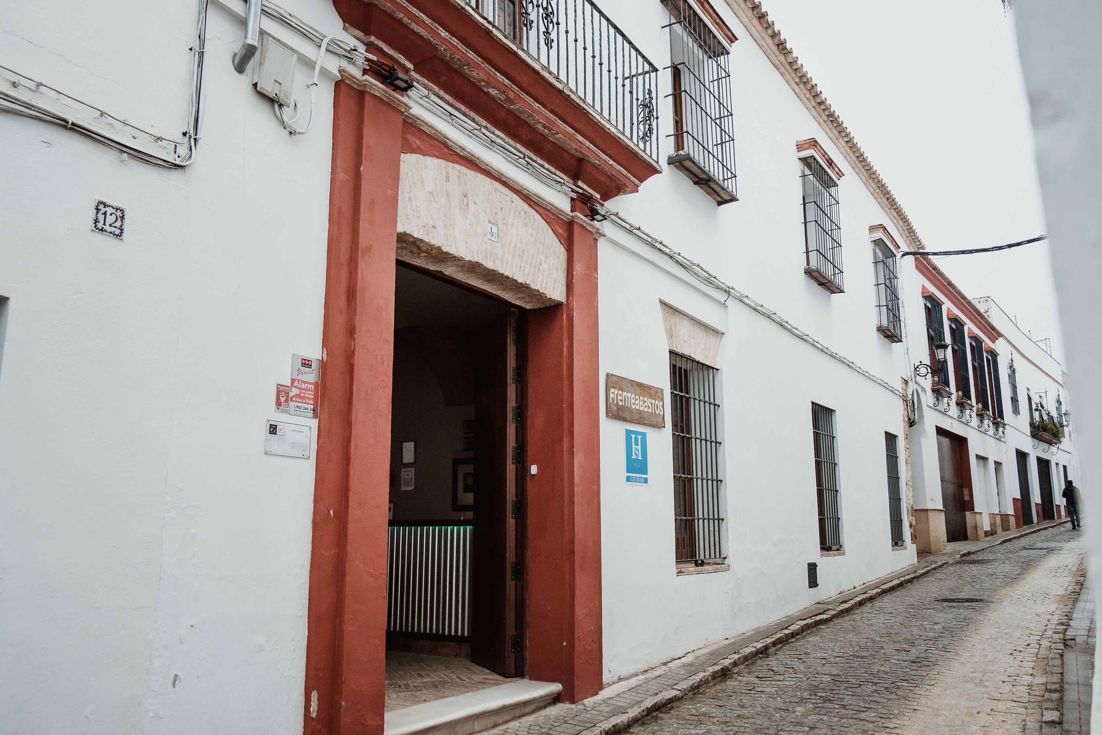 Un edificio blanco con entrada roja, un letrero que dice "Frente a la Plaza" y una calle empedrada.