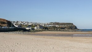 A coastal town with a sandy beach, houses on a cliff, and a clear sky. - The Cottage at Cromlech Manor Farm (Tyn-y-Gongl)