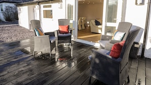 An outdoor deck with wicker furniture and a glass door leading to an interior space with a dining area. - The Cottage at Cromlech Manor Farm (Tyn-y-Gongl)