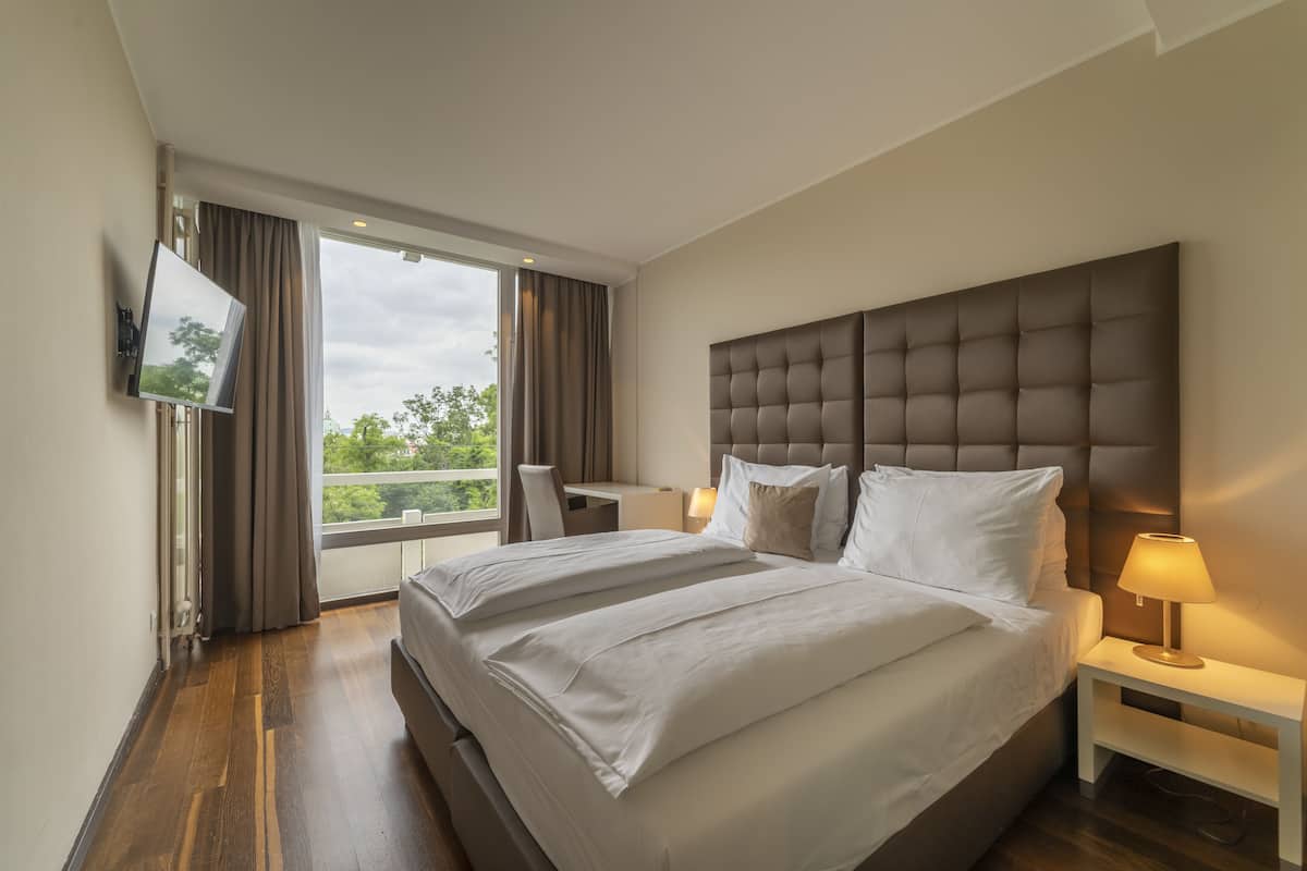 A modern hotel room with a large bed, a desk, and a TV mounted on the wall.