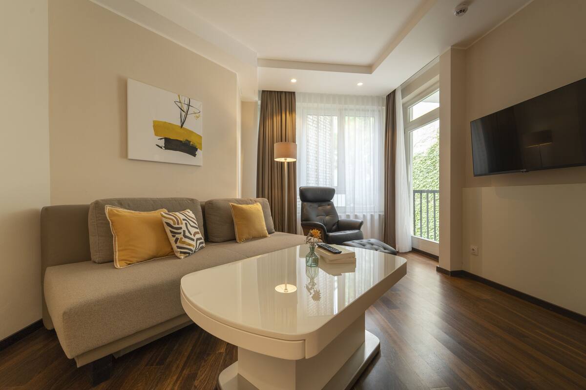 A modern living room with a sofa, a coffee table, a TV, and a window with curtains.