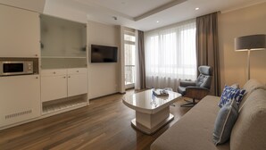 Una sala de estar moderna con un sofá, una mesa de centro, un televisor montado en la pared y una zona de cocina con armarios y un microondas.