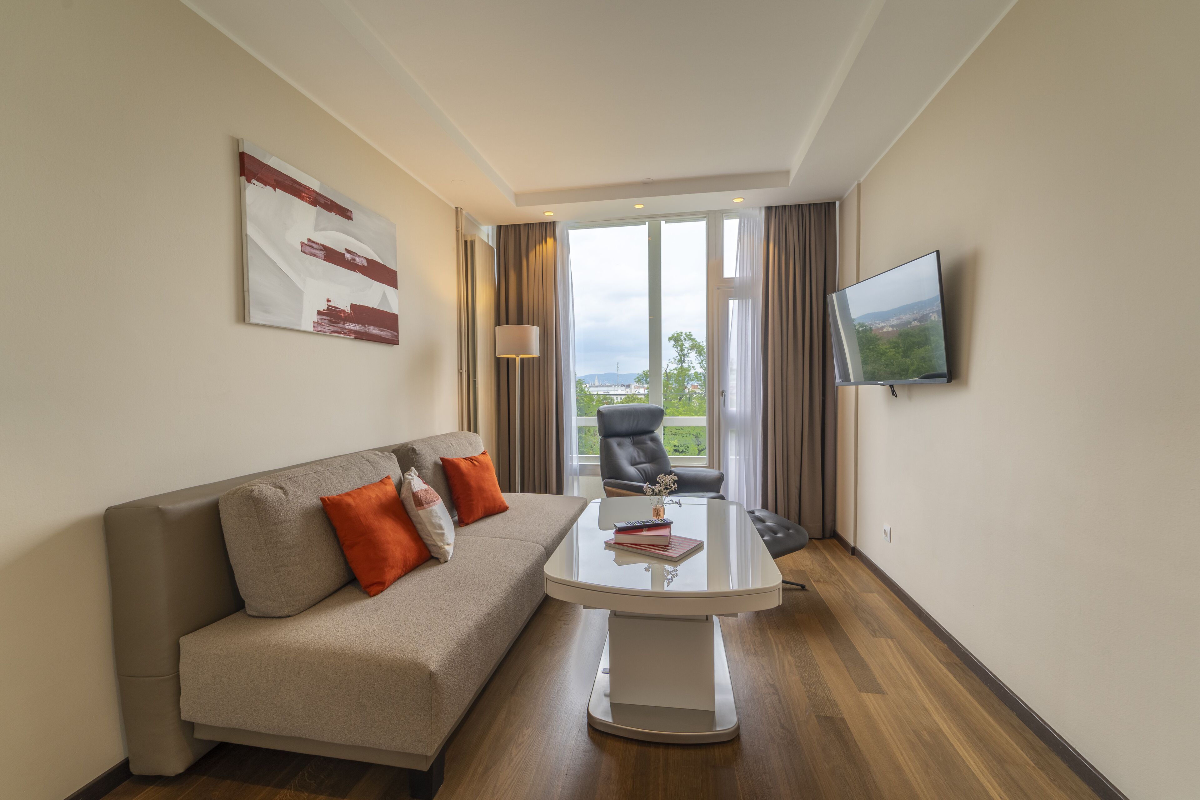 Una habitación de hotel moderna con sofá, una mesa de centro, televisor y vistas al exterior.