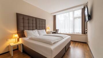 Una habitación de hotel moderna con una cama grande, mesitas de noche con lámparas, un televisor de pantalla plana montado en la pared y un ventanal con cortinas.