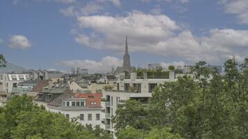 A cityscape with a prominent church spire, modern buildings, and dense greenery.