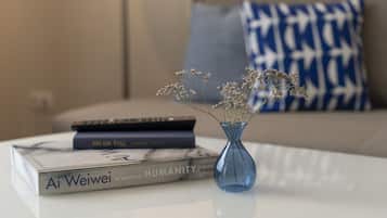 A white table with a blue vase containing dried flowers, a book titled 'Ai Weiwei: In Search of Humanity', and a remote control.