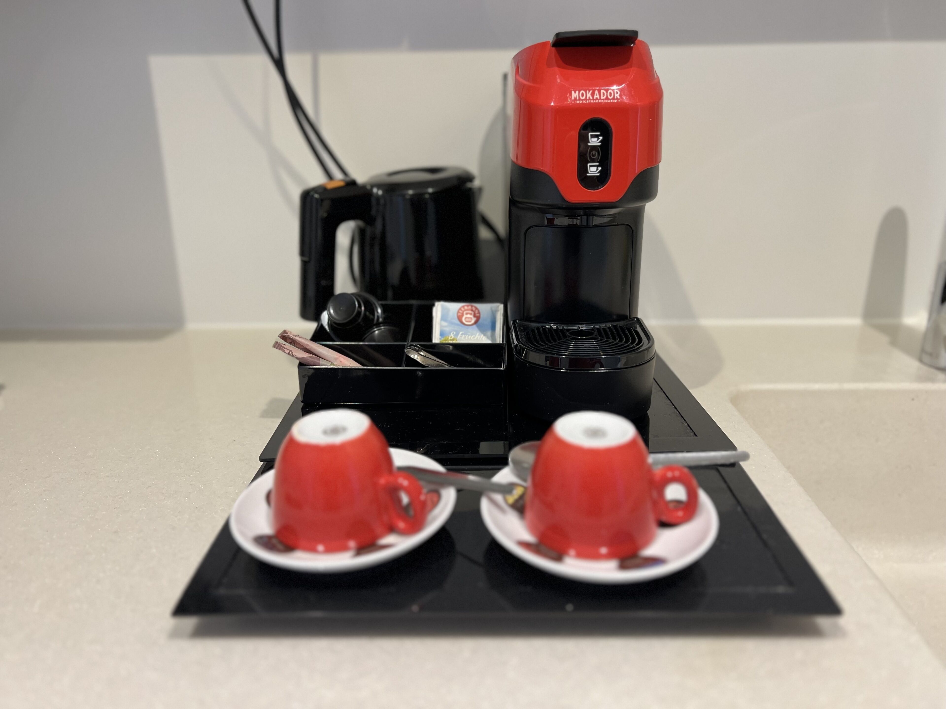 En kaffemaskine med to røde kopper på et sort fad.