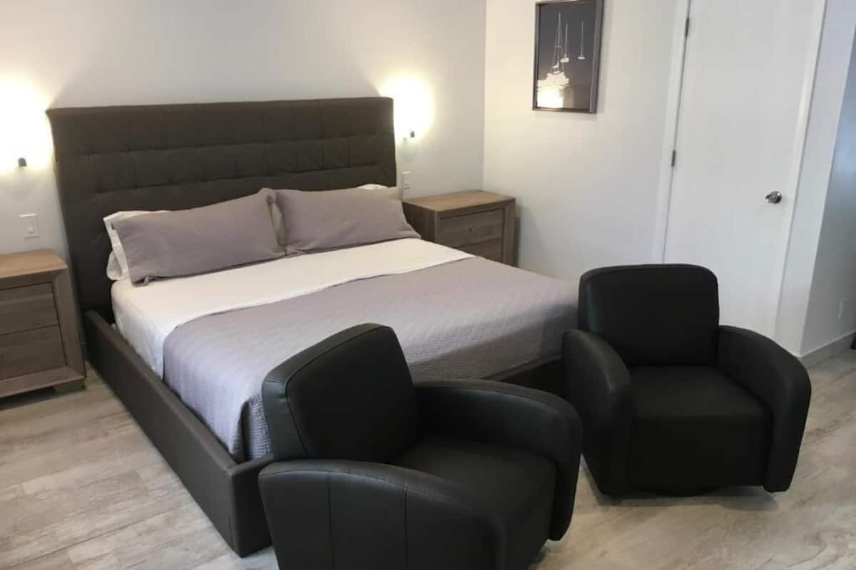 A bedroom with a large bed, two bedside tables, a nightstand, and two black chairs.