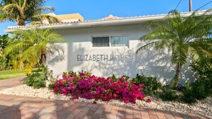 En bygning med skiltet "ELIZABETH HOUSE" og en have med lyserøde blomster og palmer.