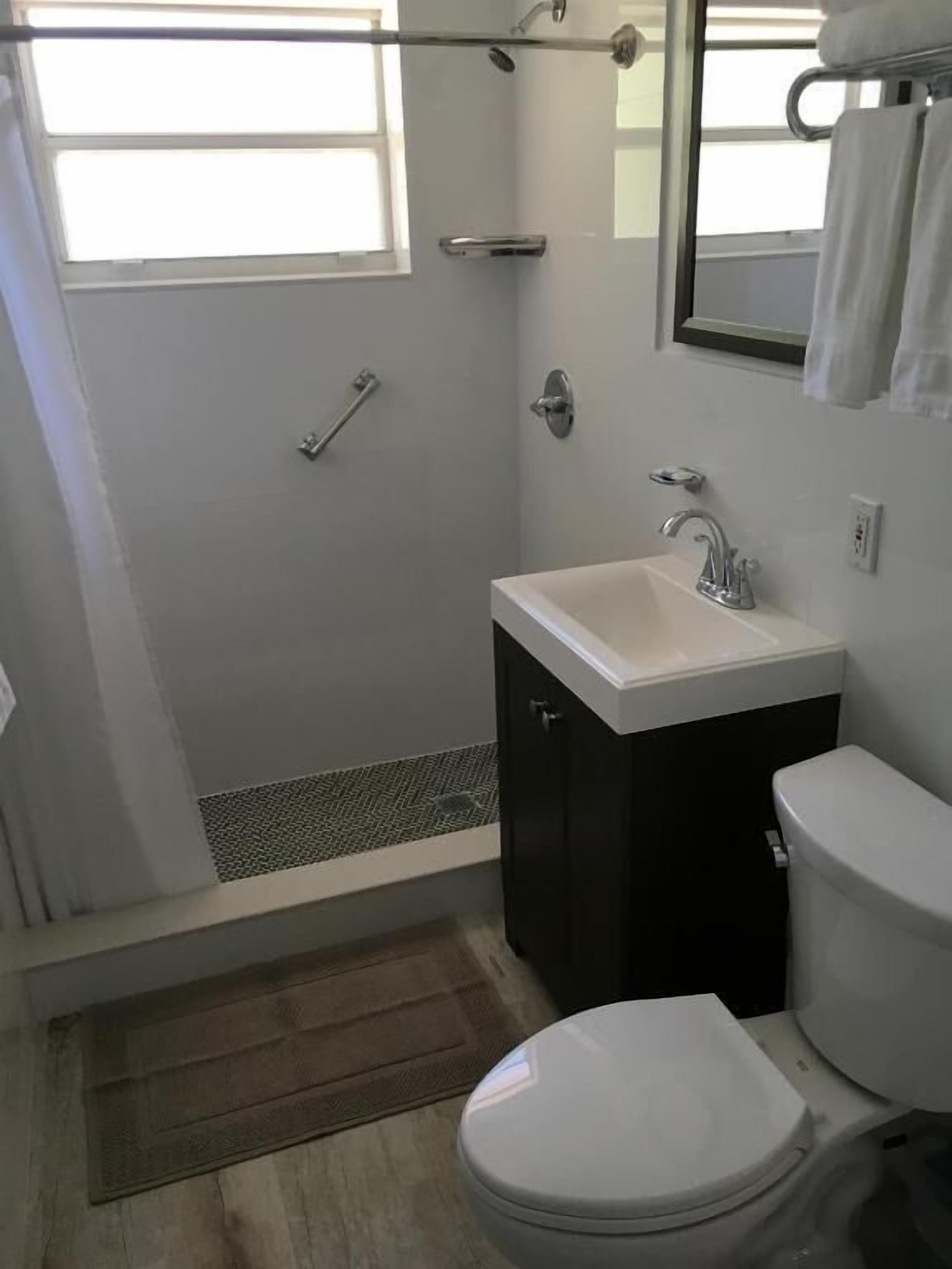 A bathroom with a shower, toilet, sink, and a window.