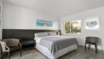 Ein modernes Schlafzimmer mit einem Bett, zwei Stühlen, einem dunklen Kopfteil und Kunstwerken an den Wänden.