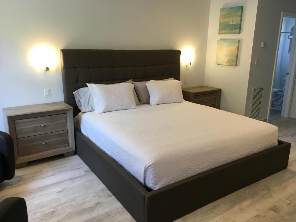 A bedroom with a large bed, two bedside tables, a nightstand, and a wall-mounted light fixture.