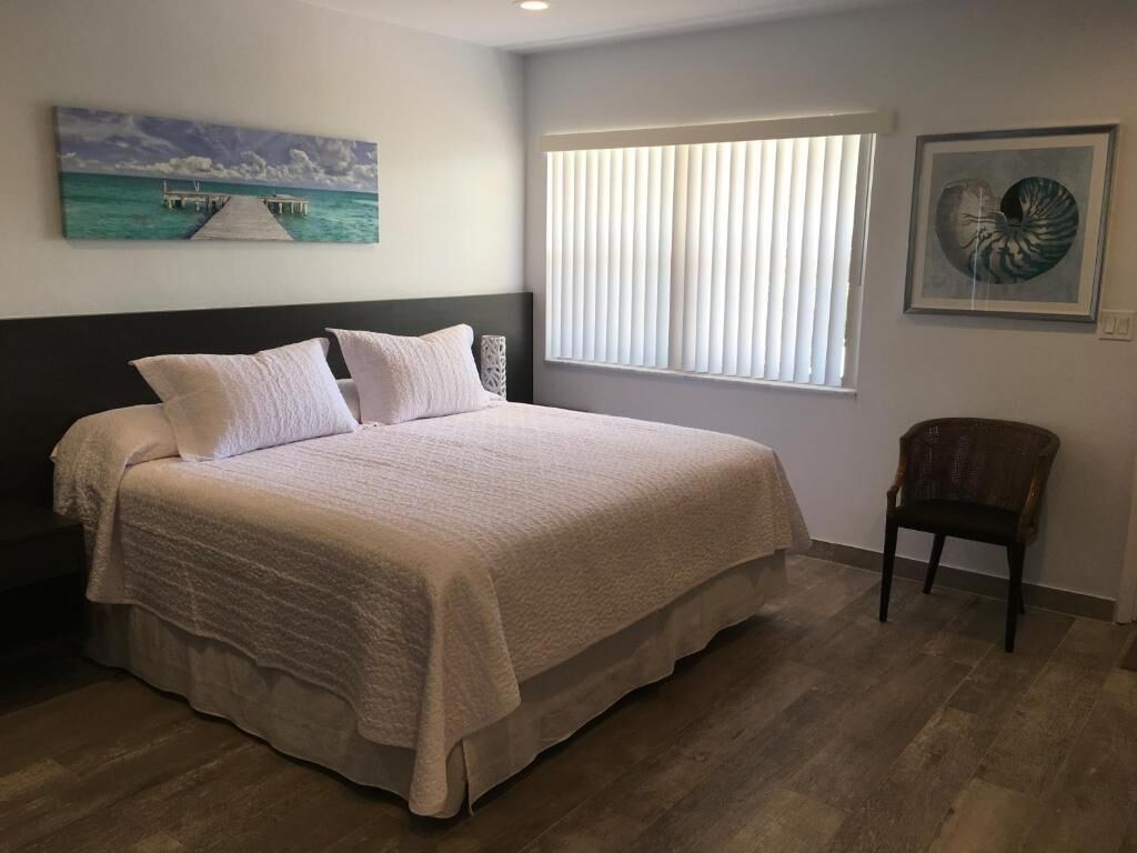 A bedroom with a bed, a window with blinds, a chair, and artwork on the walls.