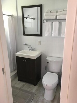 Une salle de bain avec un lavabo blanc, un meuble sombre, des toilettes blanches et un porte-serviettes avec des serviettes pliées.