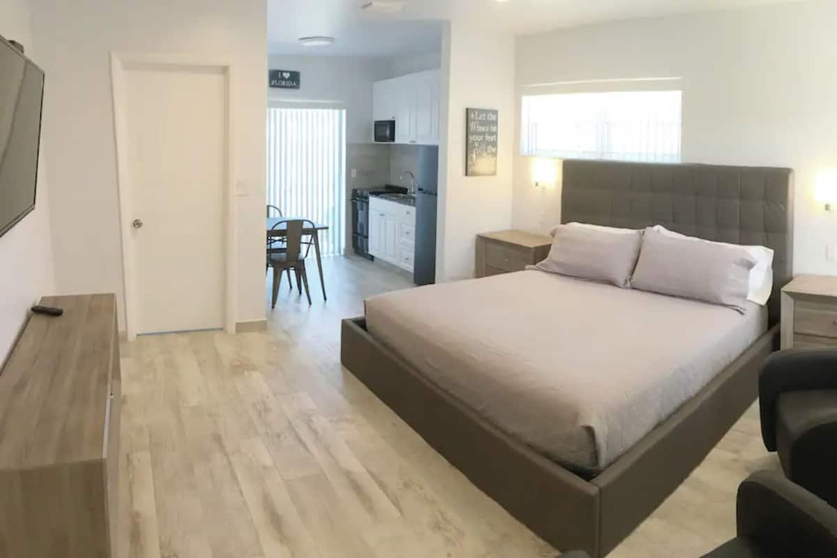 A bedroom with a bed, bedside tables, a chair, a desk, and a kitchenette.